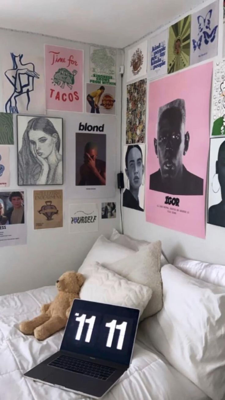 a laptop computer sitting on top of a bed in a room with posters above it