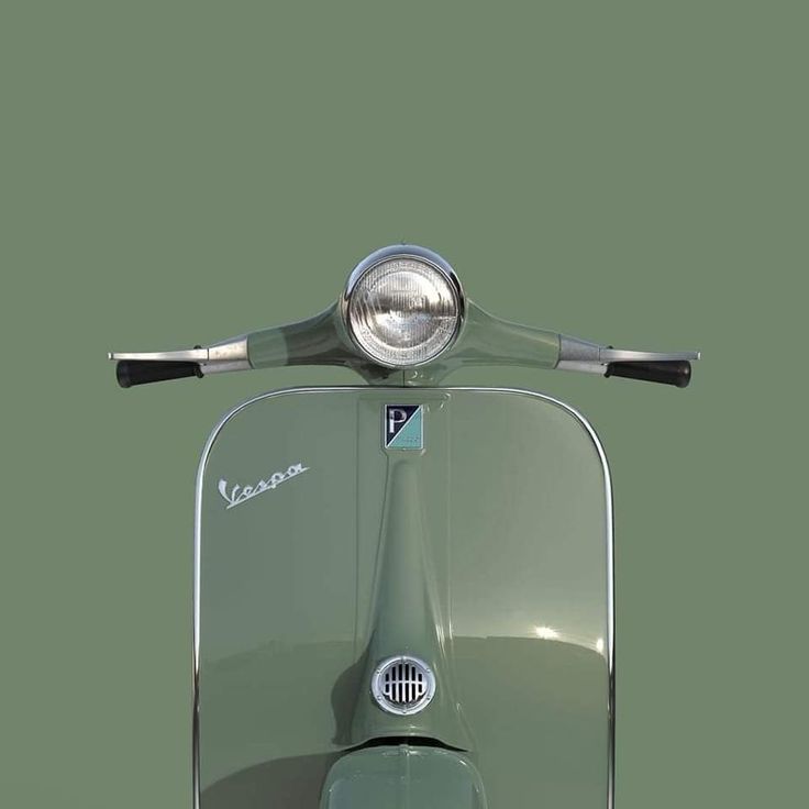 the front view of a vespa scooter on a green background with its lights on