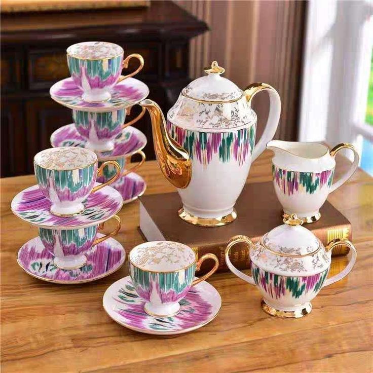 an assortment of tea cups and saucers on a wooden table with gold trimmings