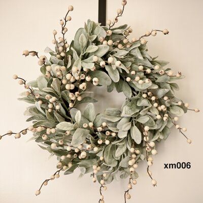 a wreath with white berries and green leaves hanging on a wall next to a cross