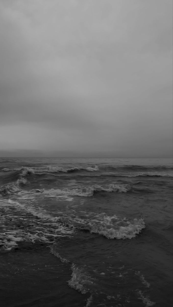 black and white photograph of ocean waves on cloudy day with dark sky in the background