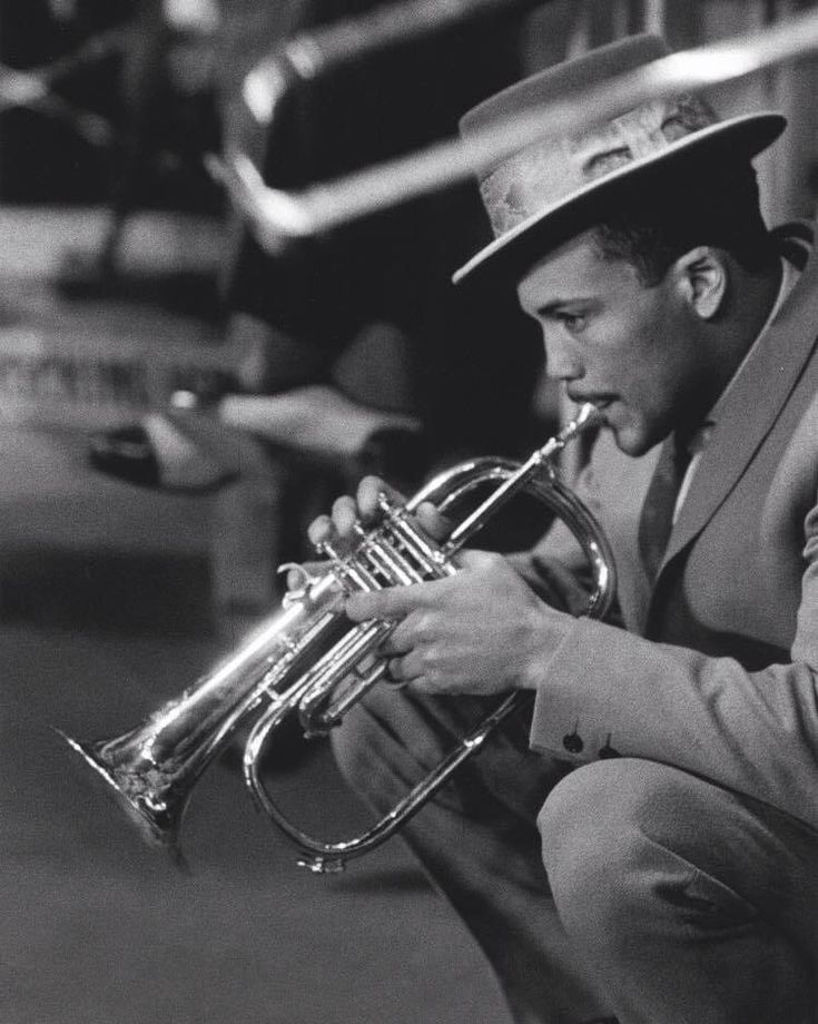 a black and white photo of a man in a hat playing a trumpet with the words quincy jones on it