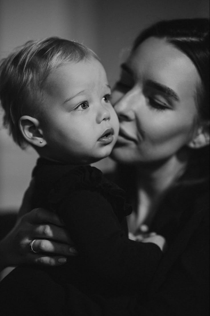 a woman holding a small child in her lap and kissing the baby's cheek