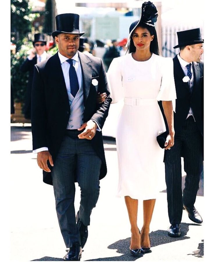 two men and a woman walking down the street wearing hats, suits and dresses with tails