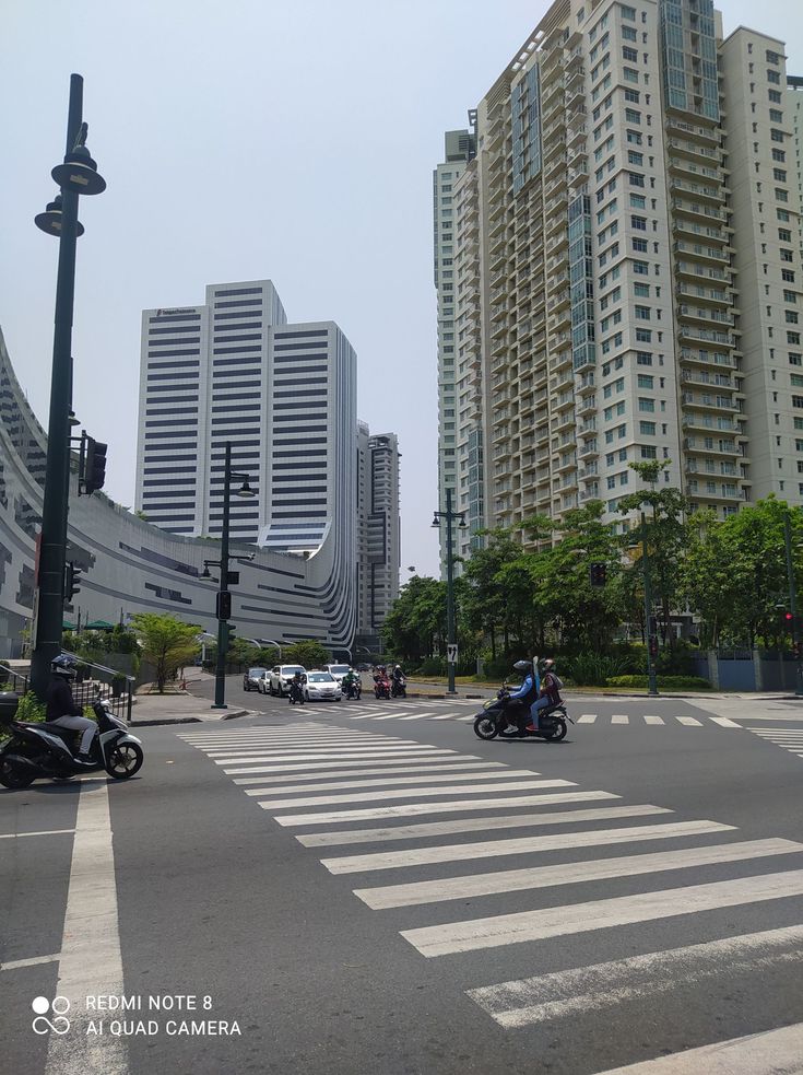 two motorcyclists are driving down the street in front of tall buildings