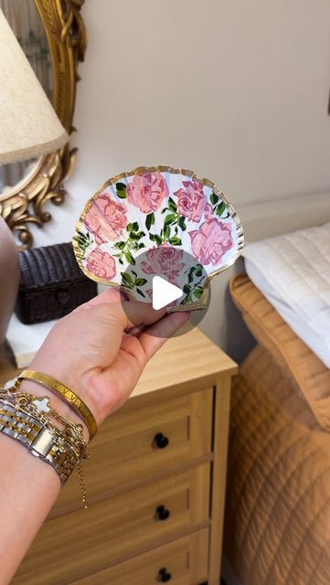 a hand holding a paper plate with flowers on it in front of a bed and dresser