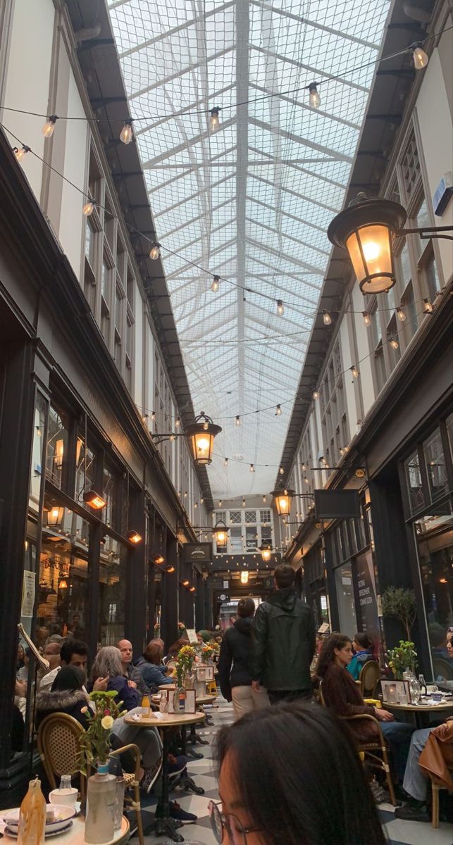 people are sitting at tables in the middle of an indoor dining area with glass ceilings