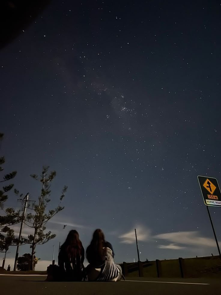 two people sitting on the ground looking up at the stars