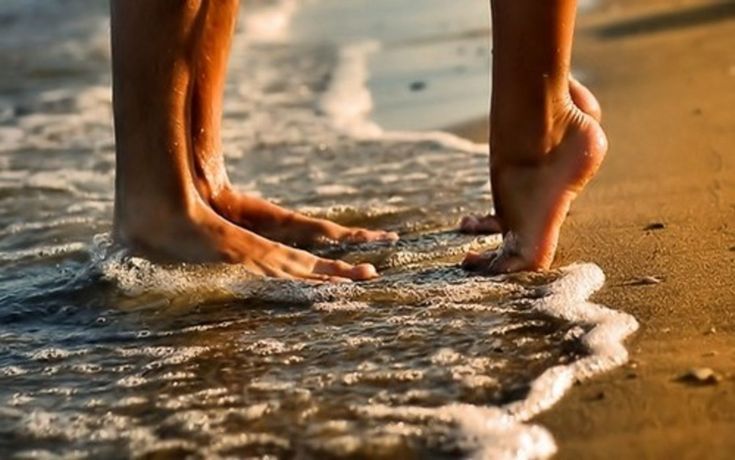 two people walking on the beach with their bare feet in the water and waves coming up to them