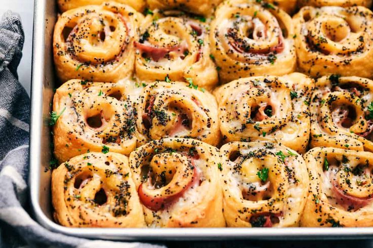 a pan filled with ham rolls covered in cheese and sprinkled with parsley