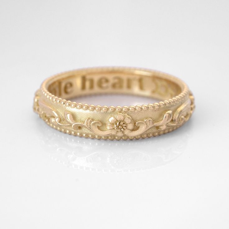 a gold ring with the word be heart engraved on it's side, sitting on a white surface