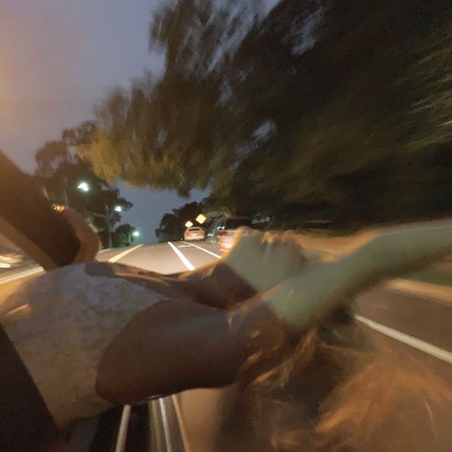 a person riding in the back of a car on a road at night with trees and street lights