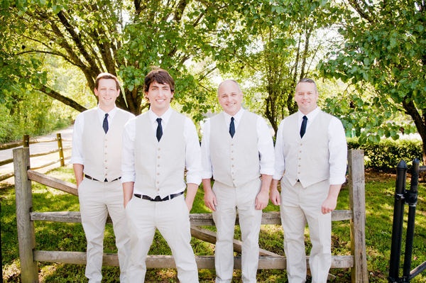 four young men in white suits and ties standing next to each other near a fence