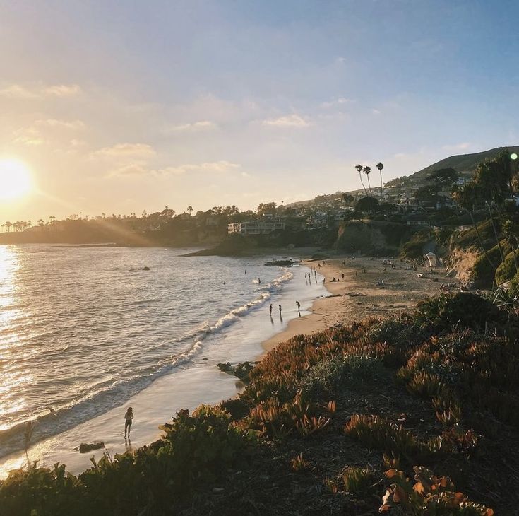 people are walking on the beach at sunset