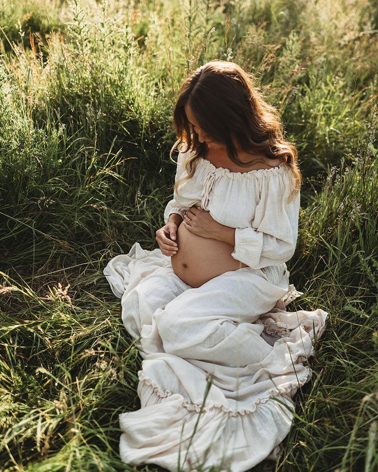 a pregnant woman sitting in the grass with her belly wrapped up and looking down at her stomach