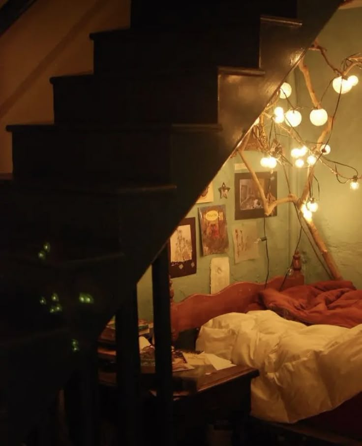 a bed sitting under a stair case next to a wall with pictures on it and lights hanging from the ceiling