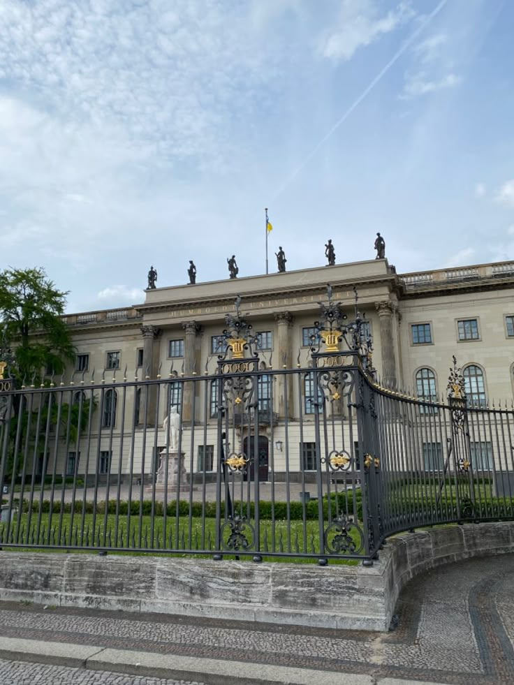 an old building with iron gates and statues on the front gate, surrounded by green grass