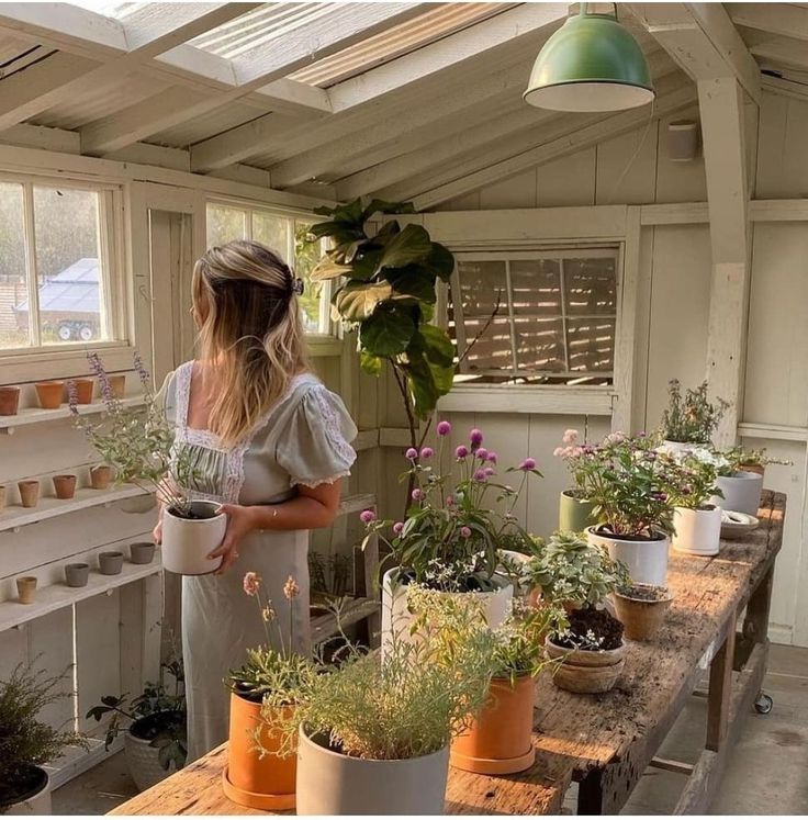 a woman holding a potted plant while standing in a room filled with pots and plants