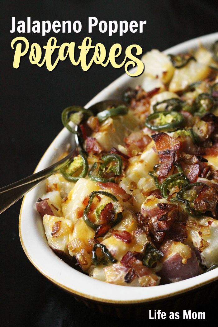 a bowl filled with potatoes and bacon on top of a black table next to a spoon