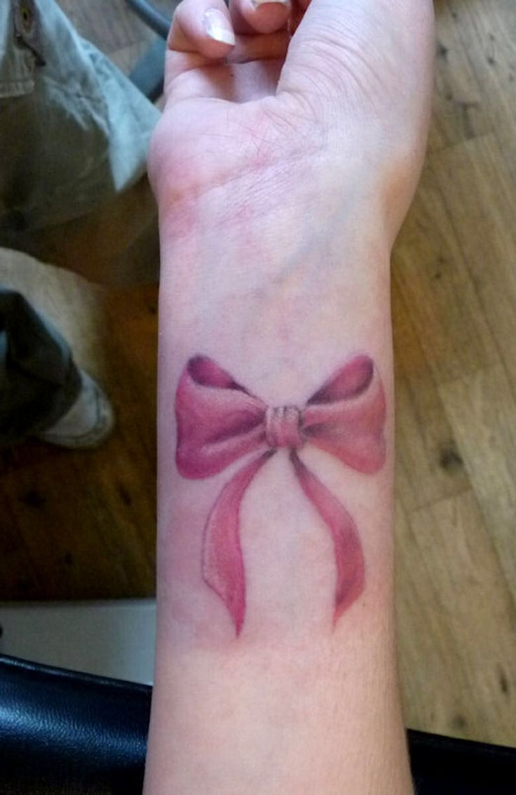 a woman's arm with a pink bow tattoo on it, and the wrist