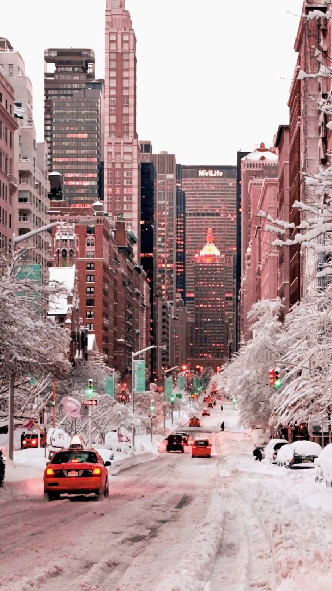 cars driving down a snow covered street in the middle of tall buildings and skyscrapers