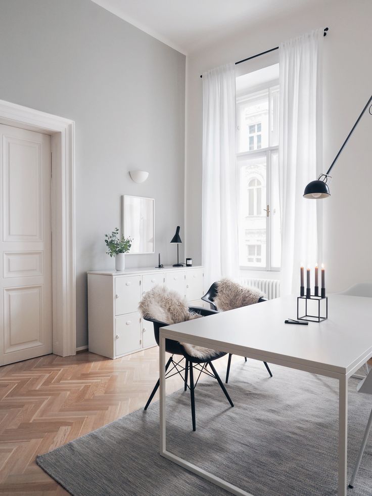 a living room with white walls and wooden flooring is pictured in this image, there are two chairs at the end of the table