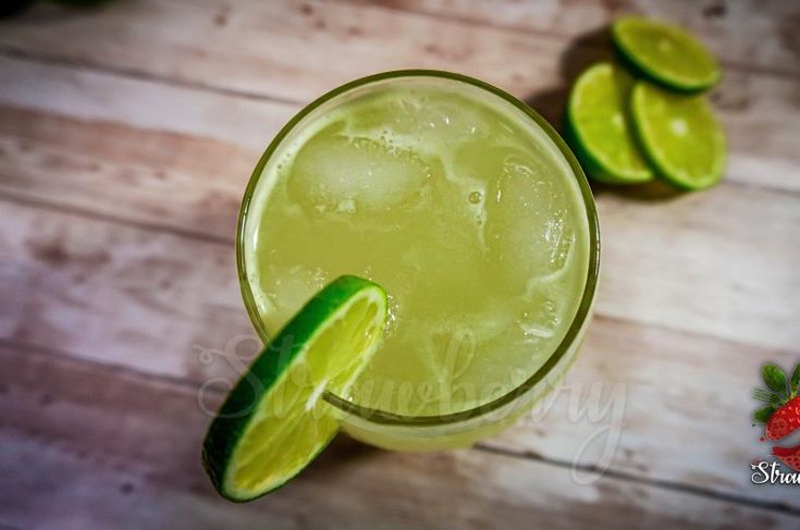 a close up of a drink on a table with limes and strawberries around it