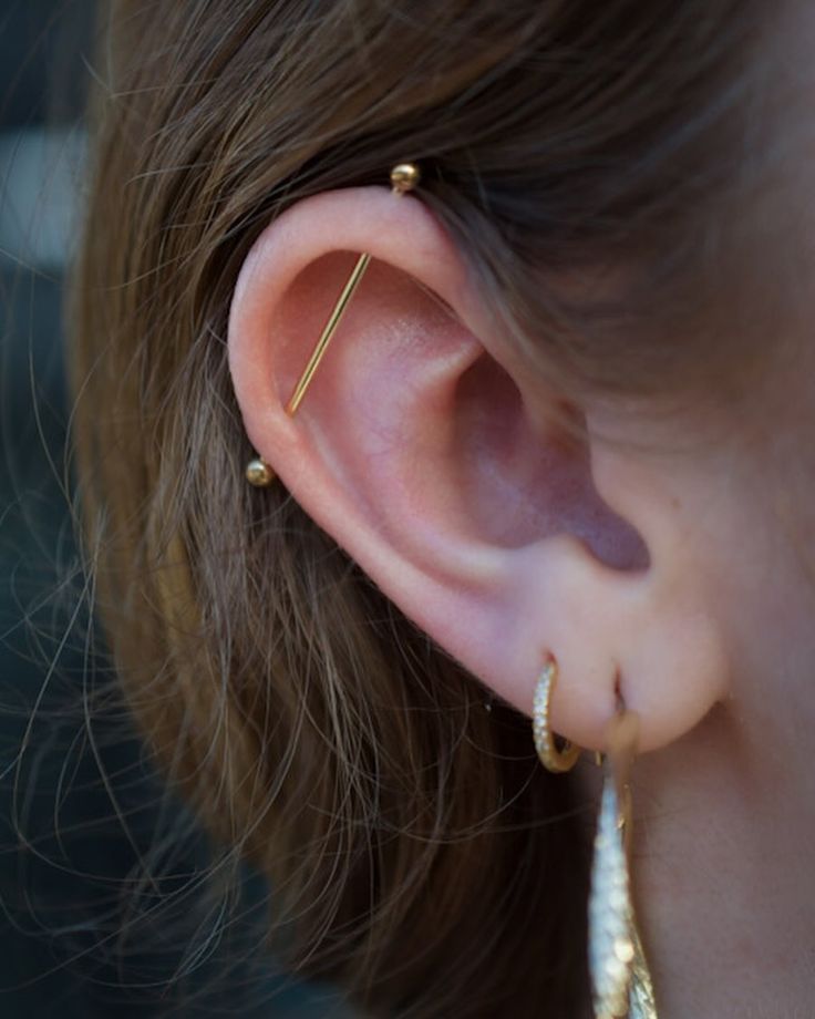 a close up of a person wearing gold ear piercings and earrings on their ears