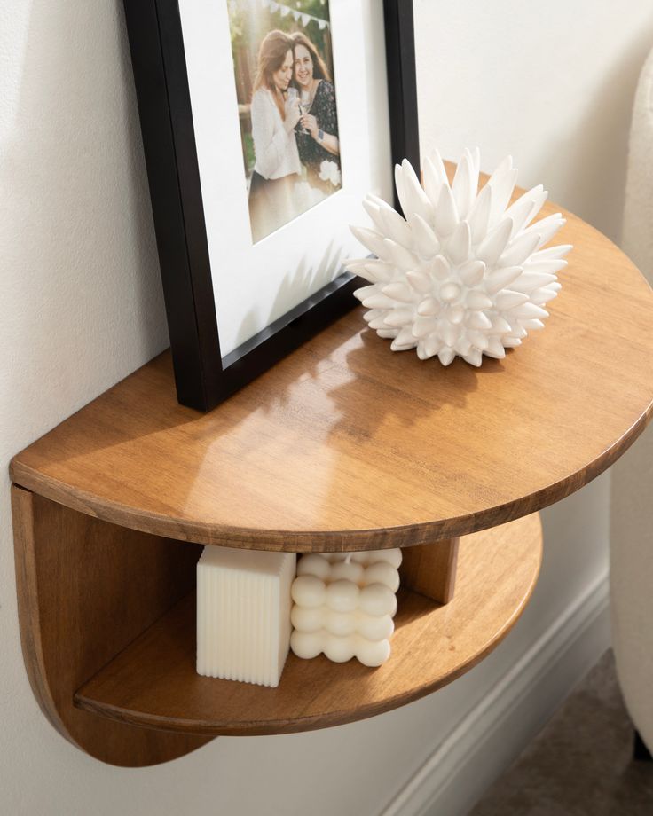 a wooden shelf with two candles and a vase on it next to a framed photo