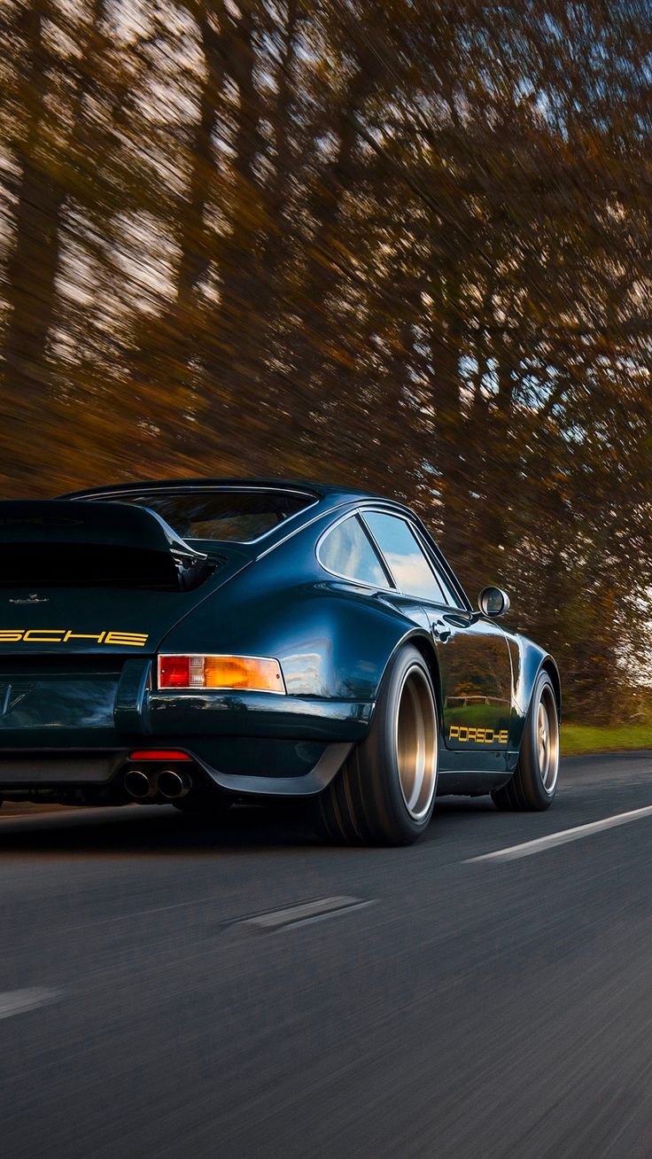 a blue sports car driving down the road with trees in the backgrouund