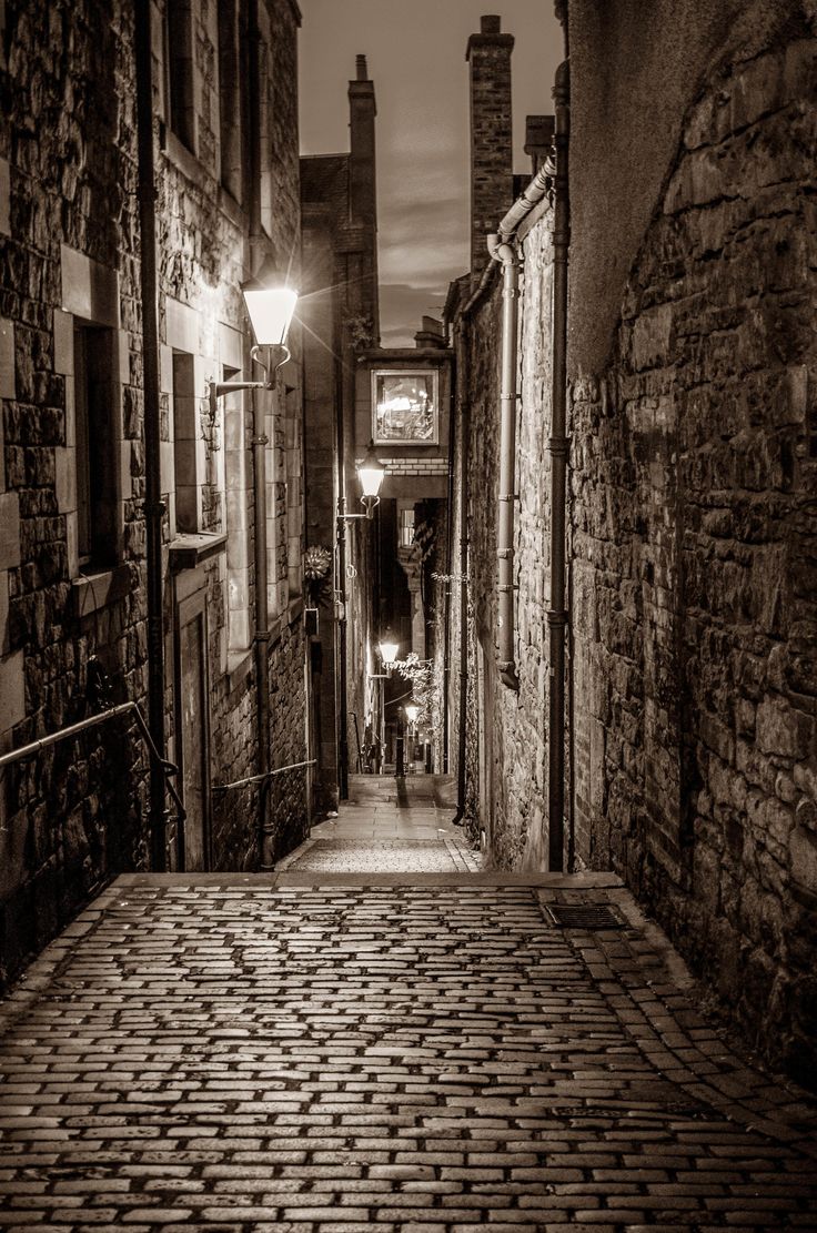 an alleyway with cobblestone pavement and street lamps on either side in black and white