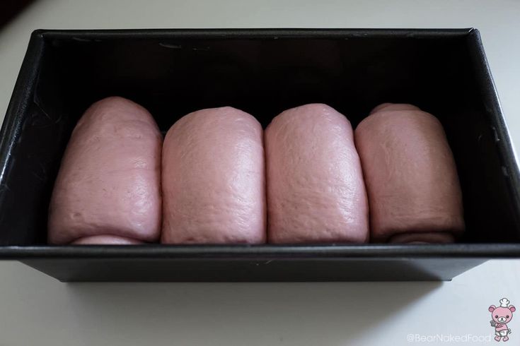 four pink donuts in a black box on a white counter top with a pig stick sticking out of it