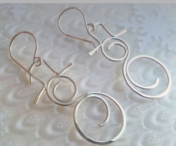 three pairs of silver earrings sitting on top of a white table covered in lacy doily