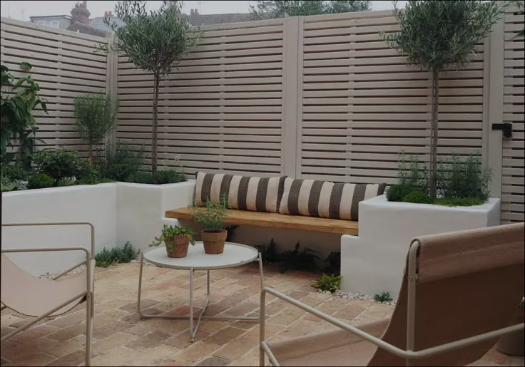 an outdoor seating area with chairs, tables and plants on the side of a fenced in backyard