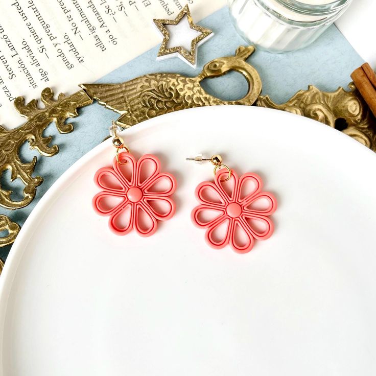 a pair of red earrings sitting on top of a white plate next to an open book