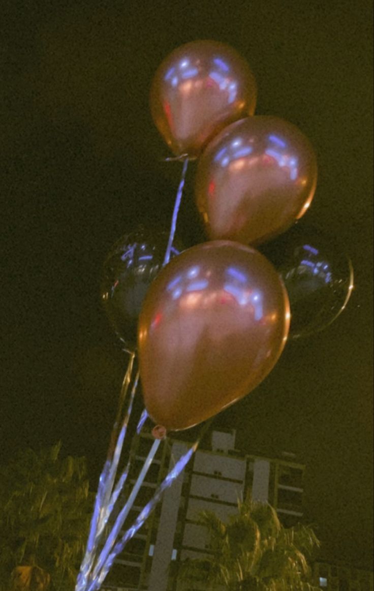 some balloons that are floating in the air at night with buildings in the back ground