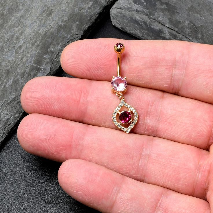 a person is holding an open belly ring with two different colored stones on the side