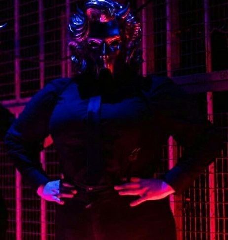 a woman wearing a mask standing in front of a caged area with neon lights