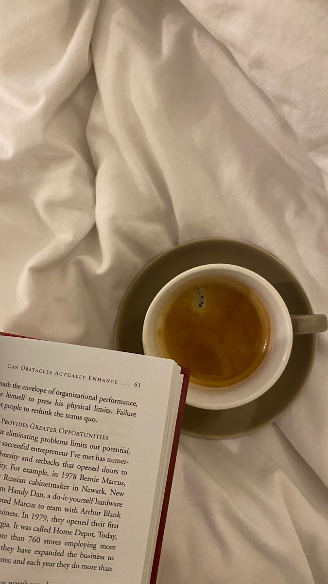 an open book sitting on top of a bed next to a cup of coffee and saucer