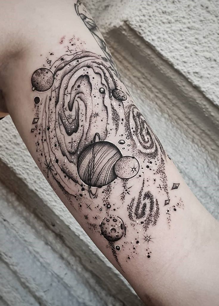 an arm tattoo with planets and stars on the outer half of it, in black ink