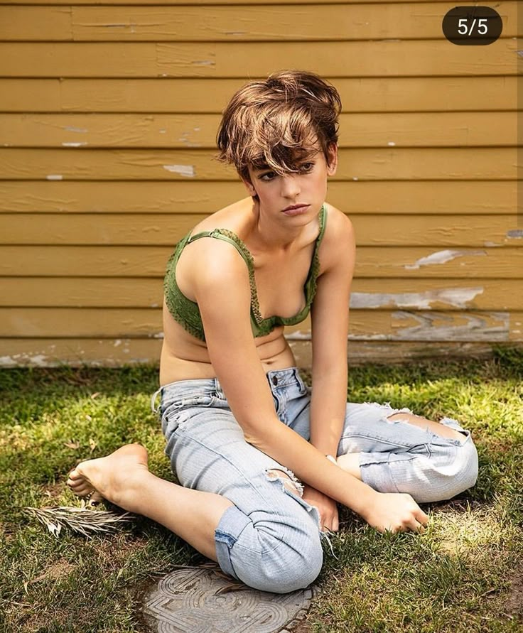 a young woman sitting on the ground in front of a house with her legs crossed