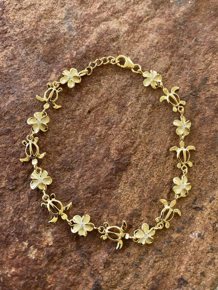 "8MM PLUMERIA & TURTLE GOLD PLATED STERLING SILVER BRACELET This genuine yellow gold plated sterling silver bracelet features the Hawaiian Plumeria Flower and Hawaiian Sea Turtle. Plumeria, in Hawaiian culture symbolizes beauty, charm, grace, and new beginnings, or re-birth. It is one of the most popular flowers on the Hawaiian Islands and widely used in lei making and jewelry designs. The Hawaiian Sea Turtle, or \"Honu,\" symbolizes good luck, endurance, and long life. They are also known as \" Hawaiian Gift Ideas, Gold Flower-shaped Jewelry With Lobster Clasp, Hibiscus Flower Jewelry, Yellow Gold Bracelet With Charms, Gold Hallmarked Flower-shaped Jewelry, Gold Flower Charm Bracelet Adjustable, Gold Flower Charm Bracelet With Adjustable Fit, Plumeria Accessories, Hispanic Jewelry