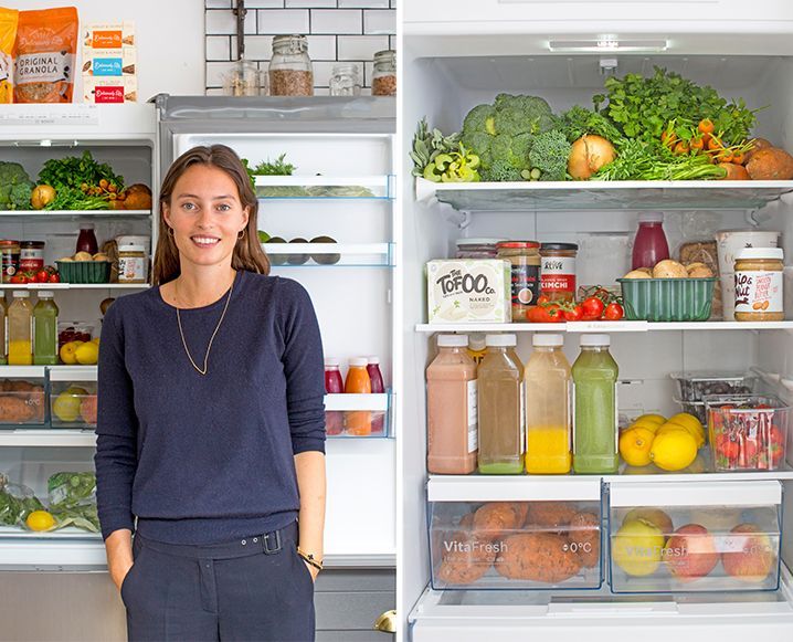 a woman standing in front of an open refrigerator filled with fruits and veggies