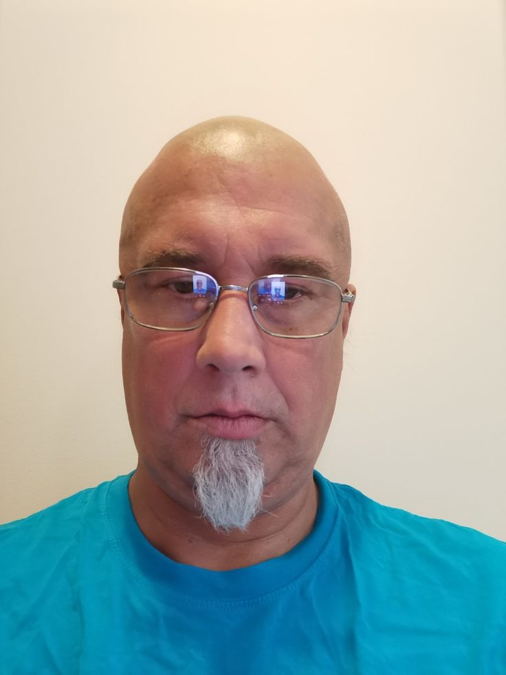 a bald man with glasses and a white beard is looking at the camera while wearing a blue shirt