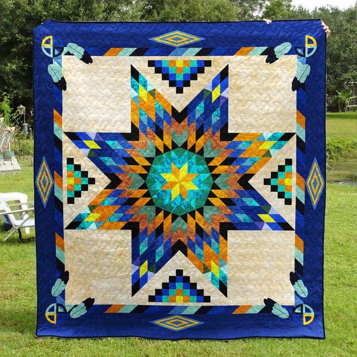 a blue and yellow quilt on grass with trees in the background