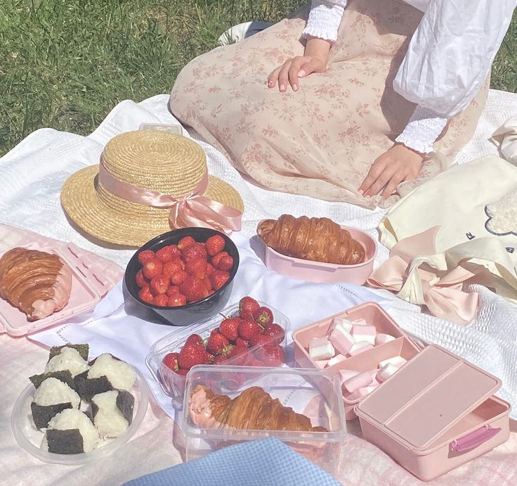 a woman sitting on the grass with some strawberries and croissants in front of her