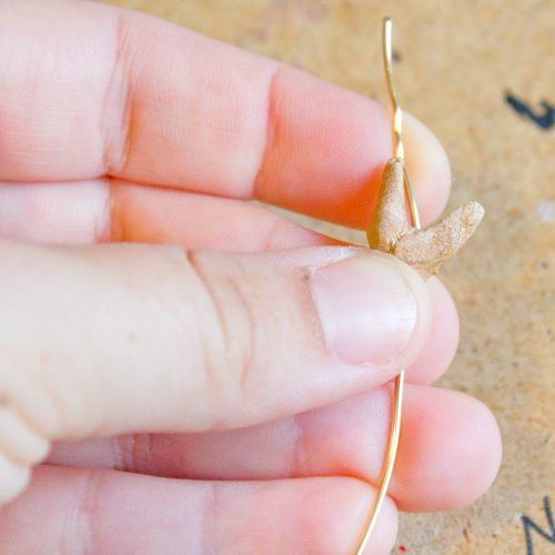 a person is holding a tiny gold bird on a thin brass wire with an arrow in the middle