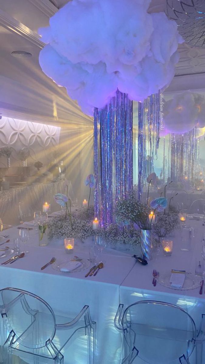 a white table topped with lots of tables covered in blue and purple lights next to tall vases filled with flowers