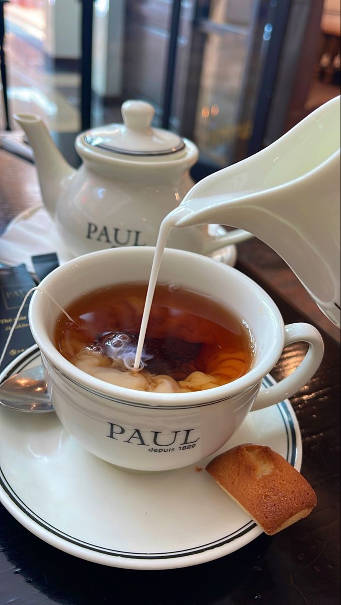 tea being poured into a white cup on a saucer with two pieces of bread next to it