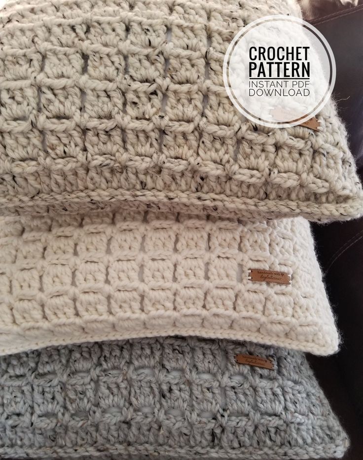 two crochet pillows sitting on top of a couch next to each other, one is white and the other is gray